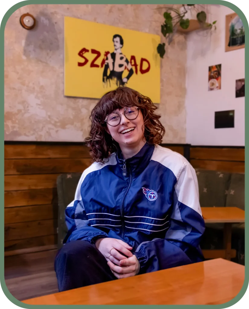Femme au centre de l'image avec une veste vintage bleu de sport. Elle à les cheveux bouclées et des lunettes. Elle se trouve dans un restaurant assise à une table. C'est votre photographe professionnelle à Lyon. 